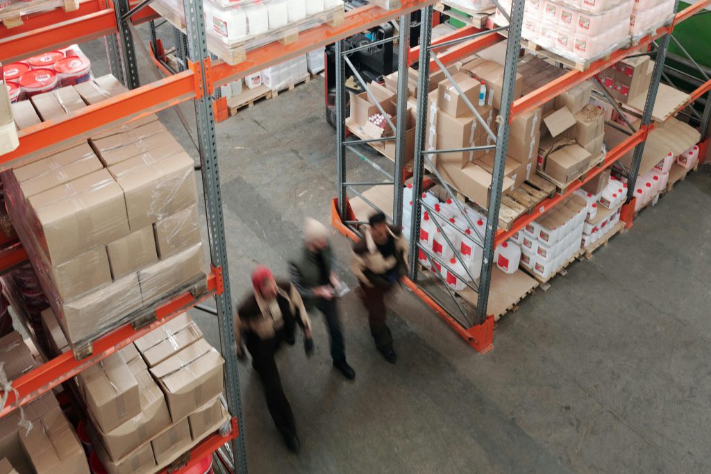 A high angle view of workers in motion in a busy warehouse with shelves full of boxes and packages.